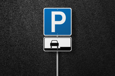 The parking road sign stands against the backdrop of asphalt, with a nearby parking area. From a top-view perspective, one can see the texture of the tarmac. Domain name monetization concept.