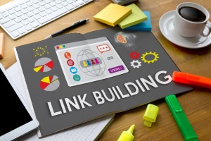 A book with the chapter title "LINK BUILDING" lies open, with color highlighters, a notebook, and a tablet nearby. The concept is quality backlinks.